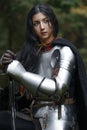 A beautiful warrior girl with a sword wearing chainmail and armor in a mysterious forest. Royalty Free Stock Photo