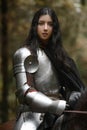 A beautiful warrior girl with a sword wearing chainmail and armor riding a horse in a mysterious forest.