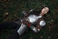 A beautiful warrior girl wearing chainmail and armor lying on the ground in a mysterious forest.