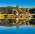 Beautiful water reflection of huge rocks and green trees with a clear blue sky Royalty Free Stock Photo