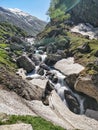A beautiful waterfall falling down through huge rocks and stones in an alpine valley with snow patches in Indian Himalayan Mounta
