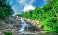 Beautiful waterfall at the mountain with blue sky and white cumulus clouds. Waterfall in tropical green tree forest. Waterfall Royalty Free Stock Photo