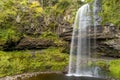 Beautiful waterfall surrounded by green foliage in a small valley (Henrhyd Falls