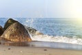 A beautiful wave hits the rocks on a sandy beach on a Sunny day