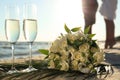 Beautiful wedding bouquet, glasses of champagne and couple on sandy beach Royalty Free Stock Photo