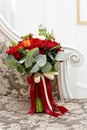 Beautiful wedding bouquet of red roses and red Hypericum berries on the sofa in the interior.
