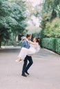 Beautiful wedding couple portrait with groom carrying his smiling bride on green park lane Royalty Free Stock Photo