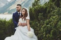 Beautiful wedding photo on mountain lake. Happy Asian couple in love, bride in white dress and groom in suit are photographed agai