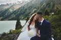 Beautiful wedding photo on mountain lake. Happy Asian couple in love, bride in white dress and groom in suit are photographed agai