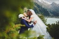 Beautiful wedding photo on mountain lake. Happy Asian couple in love, bride in white dress and groom in suit are photographed agai