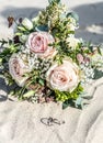 Beautiful wedding rings lie in the sand surface at the beach against the background of a bride bouquet of flowers Royalty Free Stock Photo