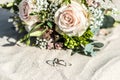 Beautiful wedding rings lie in the sand surface at the beach against the background of a bride bouquet of flowers Royalty Free Stock Photo