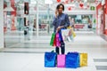 Beautiful well-dressed afro american woman customer with colored shopping bags, speaking on phone at mall Royalty Free Stock Photo