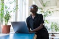 Beautiful well dressed young black businesswoman looking at the camera while sitting at her desk in her colourful office Royalty Free Stock Photo