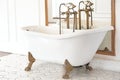 A beautiful white Baroque bathtub with gold legs and a faucet stands in a bright, spacious room next to a large mirror. Royalty Free Stock Photo