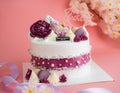 Beautiful white cake with mauve, cream and purple decorations on a pink background