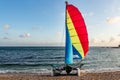 Beautiful white catamaran with red and yellow and blue sail and equipment is on the gold beach on the wet sand by turquoise sea on Royalty Free Stock Photo