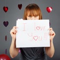 Beautiful white Caucasian blonde red haired girl woman in studio with red hearts on grey background holding a piece of paper Royalty Free Stock Photo