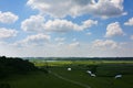 Beautiful white clouds in the blue sky. Amazing summer view on the field with shades. Green lawn and river with houses in the Royalty Free Stock Photo