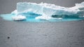 Iceberg shining in white, turquoise color in dark blue riffled Southern Antarctic Ocean, Antarctica. Penguin in foreground.