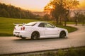 Beautiful white Nissan GTR R34 driving on a road at sunset