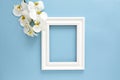 Beautiful white orchid Phalaenopsis flowers, wooden white photo frame on blue background. Top view, flat lay. Royalty Free Stock Photo