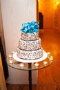 Beautiful white three-tier cake with a turquoise bow on top is on the table