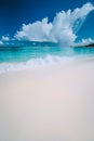 Beautiful white wave rolling towards tropical sandy beach. Gorgeous fluffy clouds above blue sea. Seychelles Grand Anse