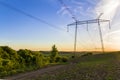 Beautiful wide panorama of high voltage lines and power pylons stretching through spring fields above group of green trees at dawn Royalty Free Stock Photo