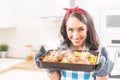 Beautiful wife holding a steaming hot tray in the kitchen, holding baked chicken and potatoes in her oven gloves, wearing apron Royalty Free Stock Photo