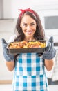 Beautiful wife holding a steaming hot tray in the kitchen, holding baked chicken and potatoes in her oven gloves, wearing apron Royalty Free Stock Photo