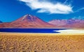 Beautiful wild arid andes high plain landscape, dark blue lake, red colorful volcano Miniques cone, sand with yellow dry grass Royalty Free Stock Photo