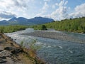 Beautiful wild Lapland nature landscape with blue glacial river, birch tree bushes, snow capped mountains and dramatic clouds.