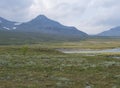 Beautiful wild Lapland nature landscape with blue glacial river, birch tree bushes, snow capped mountains Northern Sweden summer