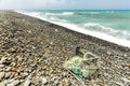 Beautiful wild rough small pebble stones beach, spoiled with rubbish - remains of black plastic box and fishing nets. Ocean Royalty Free Stock Photo