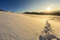 Beautiful winter Christmas landscape. Human footprint track path in crystal white deep snow through empty field, woody dark hills Royalty Free Stock Photo