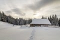 Beautiful winter landscape. Wooden shepherd hut on mountain snowy clearing among pine trees on cloudy sky copy space background. Royalty Free Stock Photo