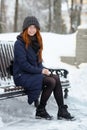Beautiful Winter Portrait Of Young Adorable Redhead Woman In Cute Knitted Hat Winter Having Fun Sitting On Bench Snowy Park