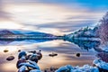 Beautiful winters day with soft clouds, snow on trees and rocks, reflections on calm water at Loch Morlich Royalty Free Stock Photo