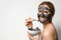 Beautiful woman applying black mask onto face against light background Royalty Free Stock Photo