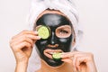 Beautiful woman applying black purifying charcoal facial mask with cucumber slices. Face skin care Royalty Free Stock Photo