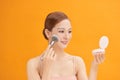 Beautiful woman applying blusher to her cheek with a large cosmetics brush while holding a compact mirror in front of her isolated Royalty Free Stock Photo