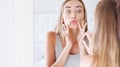 Beautiful woman applying hygienic lip balm near mirror, Attractive young woman applying lip balm and look at the mirror Royalty Free Stock Photo