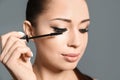 Beautiful woman applying mascara on  grey background, closeup. Stylish makeup Royalty Free Stock Photo