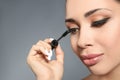 Beautiful woman applying mascara on grey background, closeup. Stylish makeup Royalty Free Stock Photo