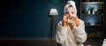 Beautiful woman applying in sheet face mask wearing bathrobe and bath towel on head looking at mirror. Cosmetological Royalty Free Stock Photo