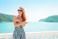 Beautiful woman applying sunscreen cream. Lady living fancy lifestyle wearing dress on holidays. Amazing view of sea and islands