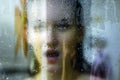Beautiful woman behind the glass with water drops looking directly at camera. Girl takes a shower, voyeurism Royalty Free Stock Photo