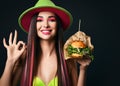 Beautiful woman big vegetarian rucola salad burger sandwich with steam smoke show ok gesture sign in green hat happy smiling Royalty Free Stock Photo