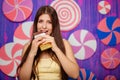 Beautiful woman bites a bar of chocolate on a background of abstract purple wall made of sweets. Royalty Free Stock Photo